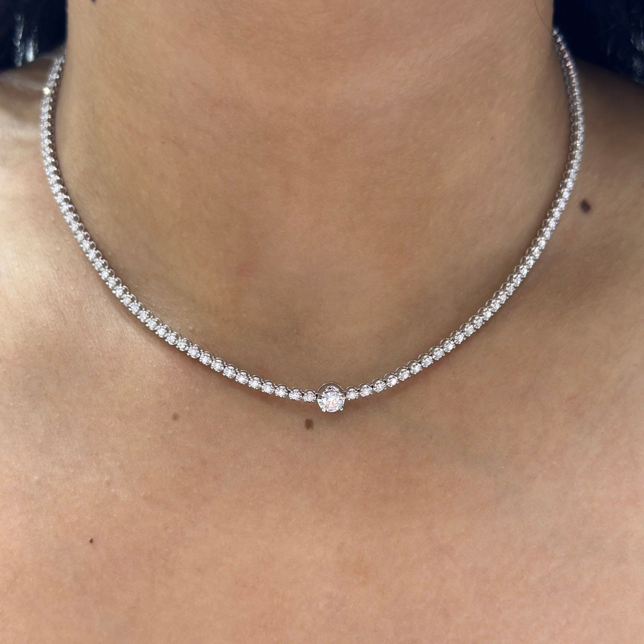 Woman wearing a diamond tennis necklace with larger carat stone in the center. (etsy image id: 6712827626)