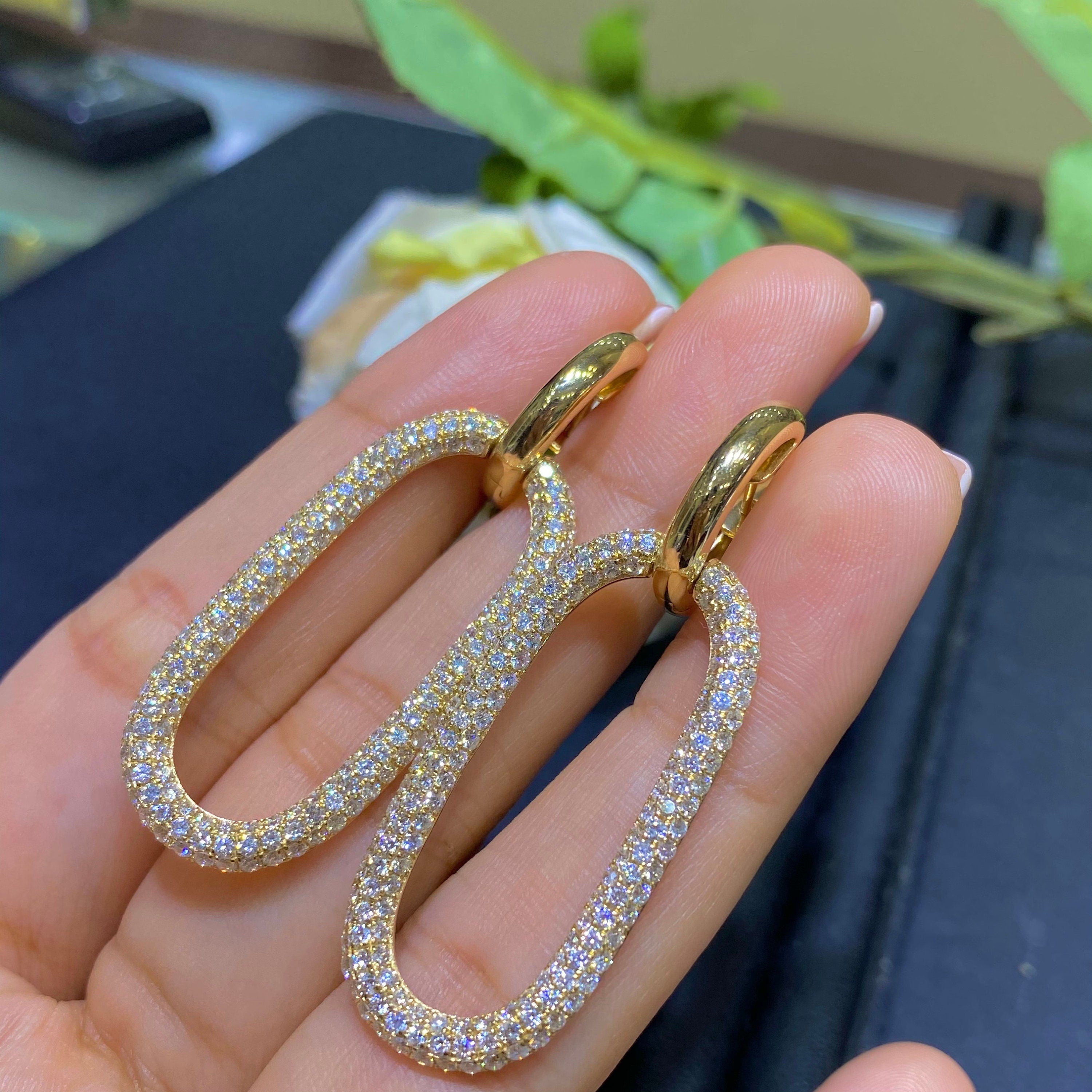 Woman holding yellow gold small hoop earrings with an elongated oval shape hoop with pave diamonds suspended off the small hoop. (etsy image id: 6758102668)