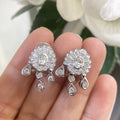 Woman holding white gold diamond cluster earrings with one center stone and multiple stones around it. (etsy image id: 6774554222)