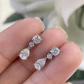 Woman holding white gold three stone diamond drop earrings. Top stone Round Cut diamond, middle stone smaller cut diamond, bottom stone pear shape diamond. (etsy image id: 6806049231)