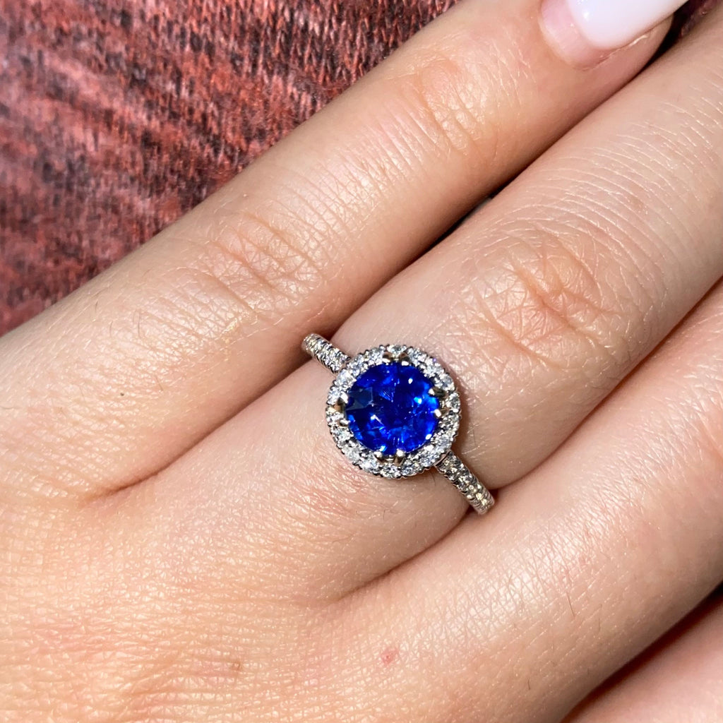 A ring with a blue sapphire center stone surrounded by a halo of smaller diamonds. The ring is set in white gold. (etsy image id: 6828817890)