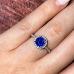 A ring with a blue sapphire center stone surrounded by a halo of smaller diamonds. The ring is set in white gold. (etsy image id: 6828817890)